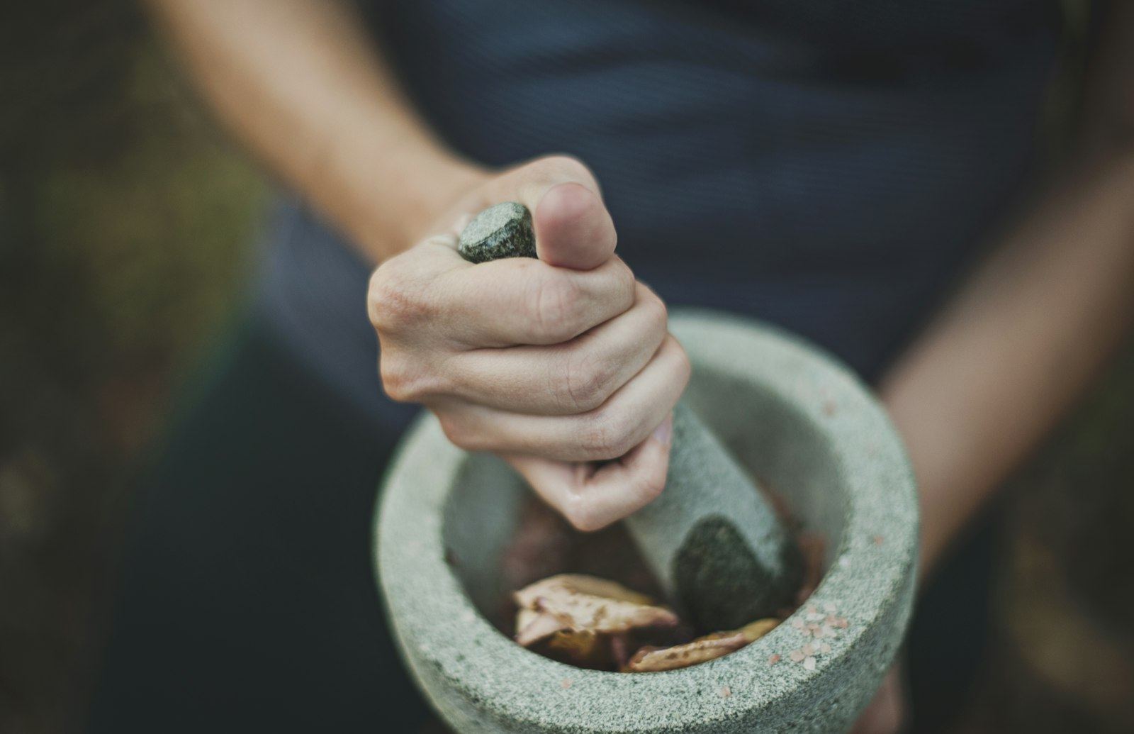 Hands grinding dried roots in a stone mortar