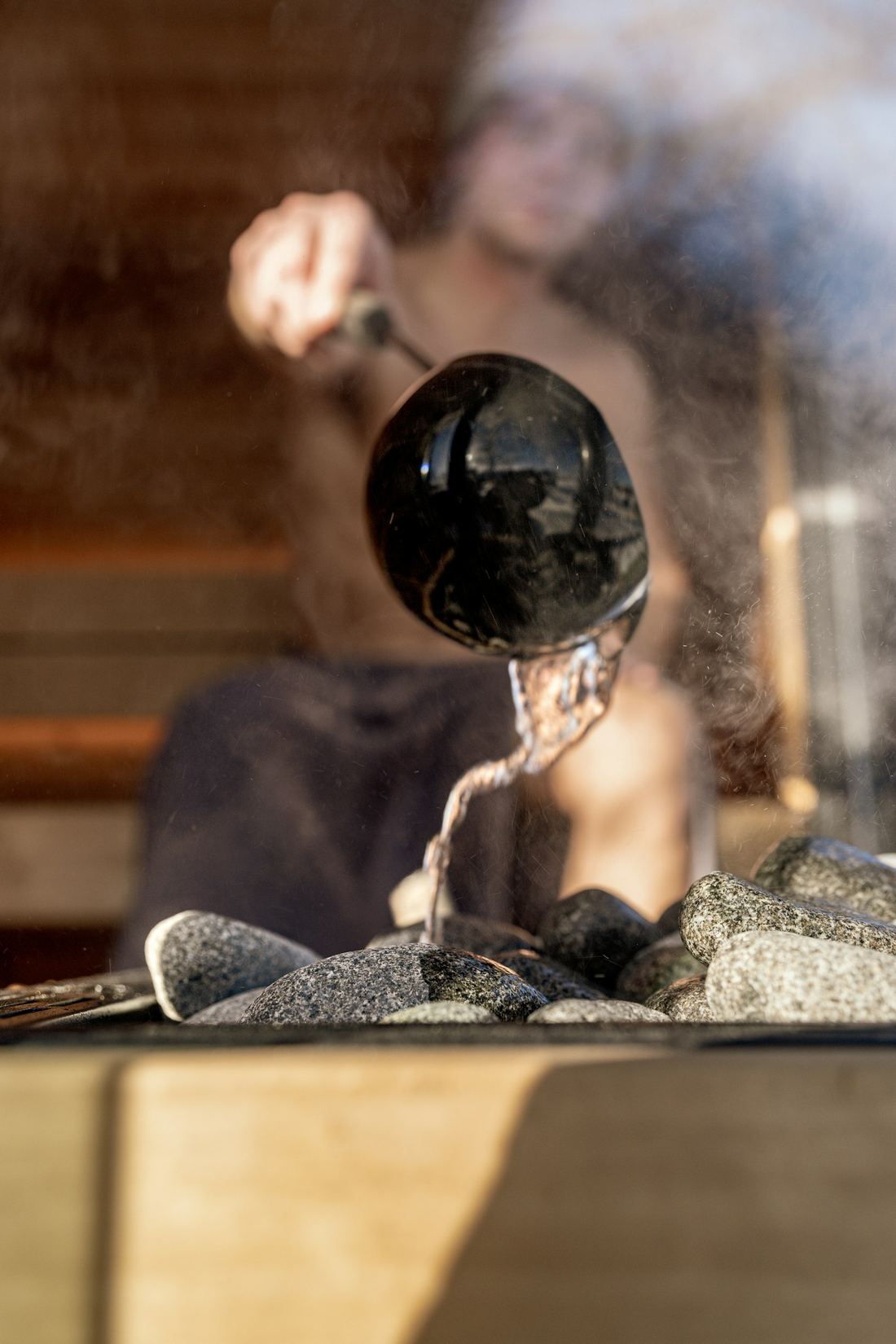 Water poured from a ladle onto sauna stones, rising as steam