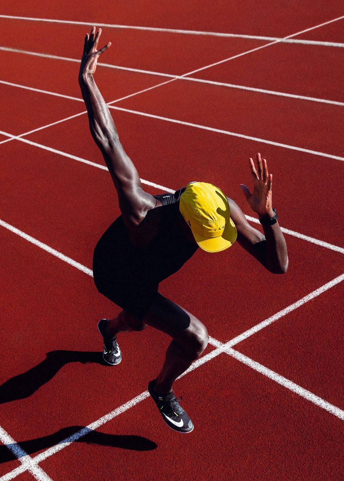 A sprinter in a yellow cap driving out of the blocks, photographed from above on a red track