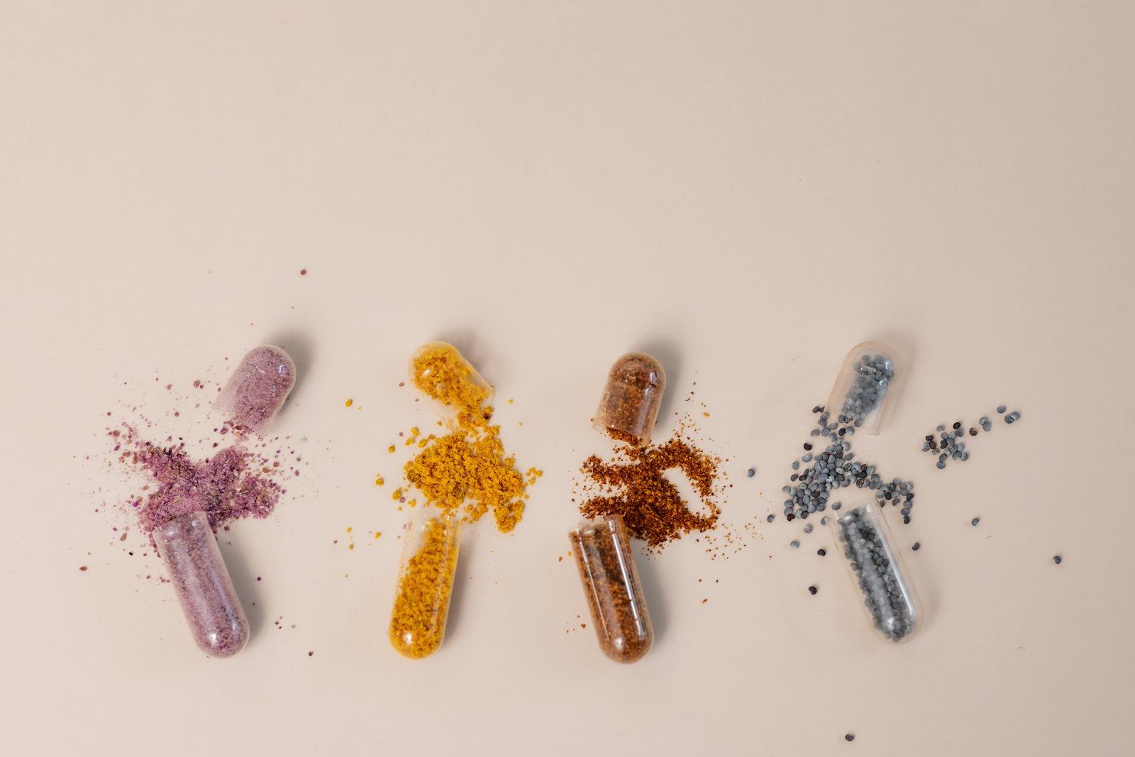 Four opened capsules spilling coloured powders onto a pale surface