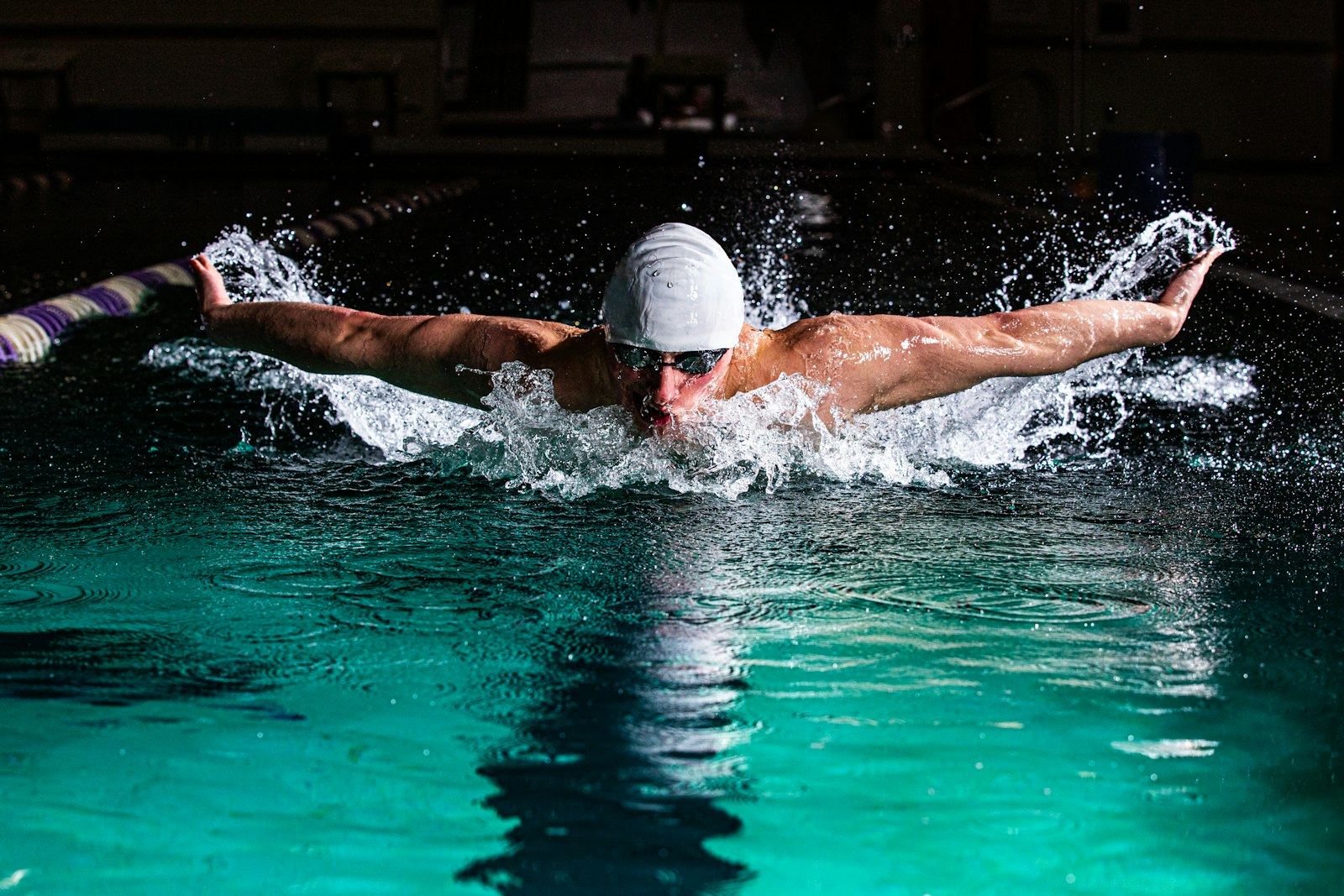 A swimmer mid-stroke in butterfly, spray lit against dark water