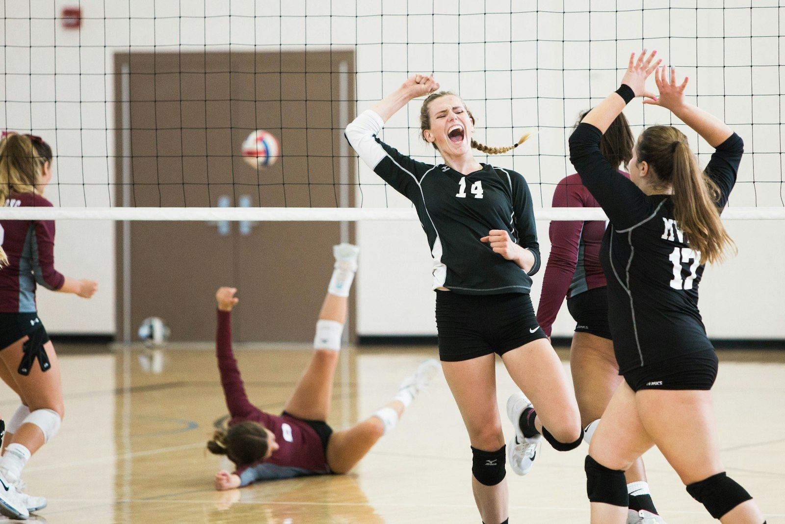 High school volleyball players celebrating a point while a teammate dives on the floor